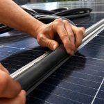 Person's hands working on a solar panel, smoothing a protective edge along a cable on the panel surface