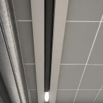 Close-up of a metal sliding door track with a narrow gap, set against a grey-tiled wall and a small rectangular light at the bottom center.